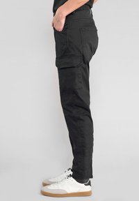 Zwarte cargobroek met een slim fit, voorzien van meerdere zakken, een gladde textuur en een enkellange pasvorm, gecombineerd met witte en grijze sneakers.
