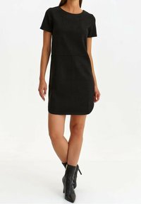 Robe noire à manches courtes avec un col rond, design ajusté, texture lisse et longueur au genou, associée à des bottines à bout pointu.