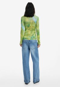 Top a maniche lunghe in tie-dye verde e blu con un design aderente, abbinato a jeans chiari a vita alta, larghi e con grandi tasche.