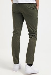 Olivgröna chinos med slim fit, tillverkade av mjukt bomullstyg. Har diskreta sömmar och sidofickor, tillsammans med vita sneakers.