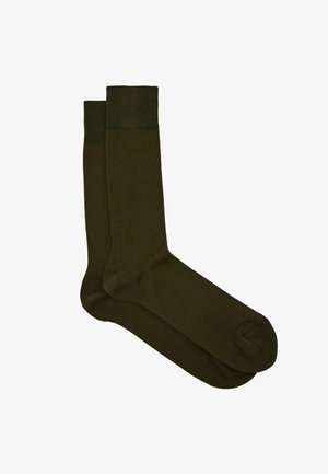 Egy pár sötét olívazöld bokáig érő zokni bordázott szegéllyel, sima textúrával és lekerekített orrterülettel, fehér háttéren fekve.