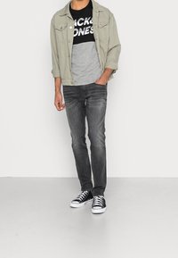 Chaqueta de mezclilla gris claro sobre una camiseta gráfica negra y gris, combinada con jeans gris oscuro y zapatillas blanco y negro.