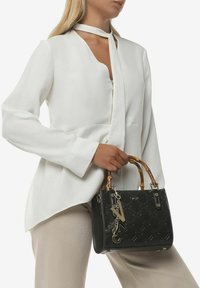 Zwarte handtas met reliëfpatroon, bamboe handvatten en metalen accenten. Draagt bij een witte top met kraag en asymmetrische snit.