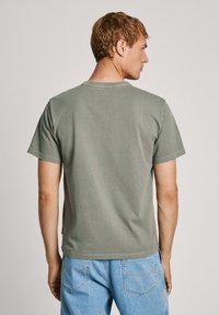 Trumpas rankovės alyvuogių žalia medvilnė t-shirt su apvalia iškirpte ir laisvu pasiuvimu. Lengvai matomas siuvimas ant rankovių ir apvado.