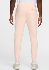 Joggers de color rosa claro hechos de tela suave, con cintura elástica, piernas ajustadas y un bolsillo trasero. Llevados con zapatillas ligeras.