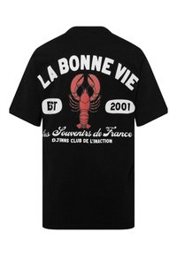 Melna T-krekls ar lielu sarkanu omāru grafiku, baltu tekstu "LA BONNE VIE," "EST 2001," un franču rakstu zem omāra.