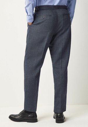Pantalones oscuros a medida de tejido texturizado. Incluye cintura con trabillas, dos bolsillos traseros y un diseño de pierna ajustada y entallada.
