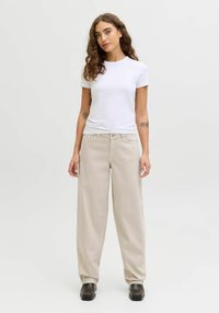 T-shirt blanc à manches courtes associé à un pantalon beige ample. Le pantalon a une coupe droite et une texture douce, complété par des chaussures marron foncé.