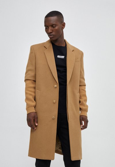 Tan wool blend coat with a tailored fit, notch lapels, ribbed sleeves, and two front pockets. Features buttons along the front.