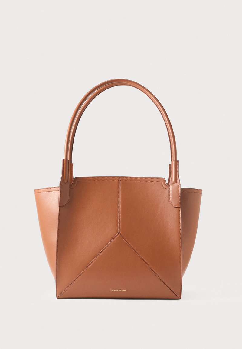 Sac cabas en cuir marron avec doubles poignées et couture géométrique sur le devant, sur un fond clair uni.