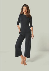 Schwarzes Stricktop mit Dreiviertelärmel und strukturiertem Muster, kombiniert mit lockeren schwarzen Hosen. Einfaches Design und weicher Stoff.