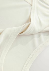 Béžový elastický body s hladkou texturou, vybavený překládaným designem a kontrastním prošíváním na okrajích. Žádné viditelné kovové prvky.