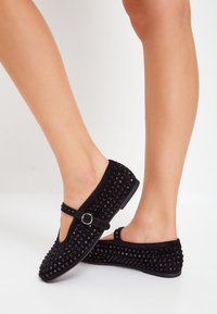 Ballerine stile Mary Jane nere realizzate in suede texturizzato con borchie nere rotonde. Presentano una cinghia con una fibbia argentata e una suola piatta.