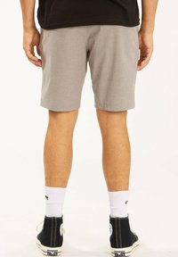 Pantalones cortos grises con un acabado texturizado, que caen justo por encima de la rodilla. Combinados con zapatillas negras de caña alta y calcetines blancos, mostrando un look casual.