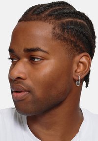 Orecchino a cerchio d'argento indossato su un orecchio forato, caratterizzato da un semplice design circolare e una superficie metallica liscia. I capelli sono acconciati in trecce.