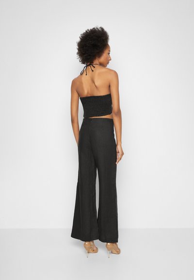 Top cropped preto com smock, combinado com calças largas pretas; modelo usa sapatos de salto nude; a vista traseira destaca a cintura e o design cropped.