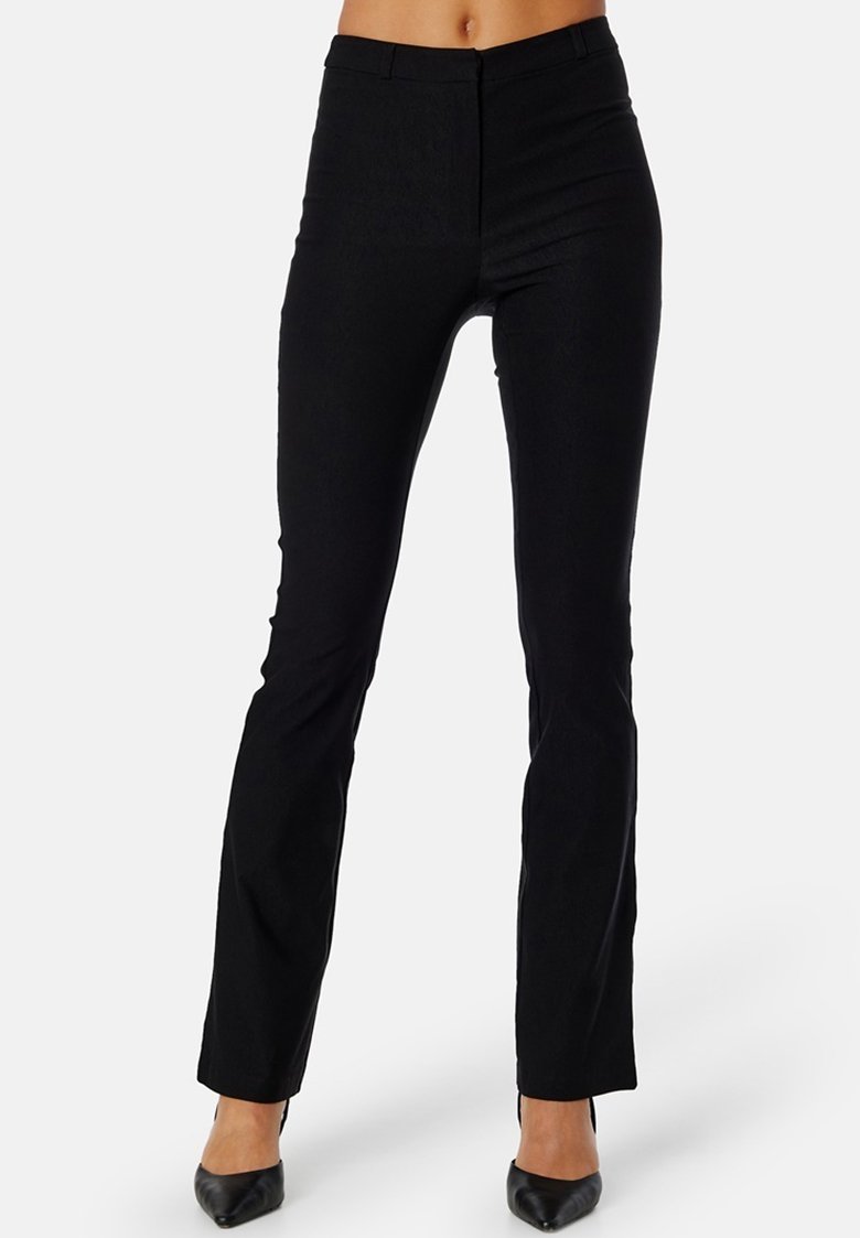 Zwarte slim-fit broek met een gladde textuur, hoge taille en subtiele details, gecombineerd met puntige zwarte hakken.