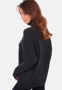 Dunkelgrauer Rollkragenpullover mit lässigem Schnitt, strukturiertem Strickmuster und geripptem Saum. Lockere Ärmel und hohes Kragen-Detail sind sichtbar.