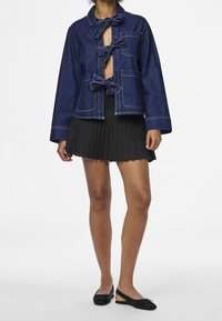 Jeansjacka med flugor, öppen front och två framfickor. Matchad med en plisserad svart kjol och svarta skor.