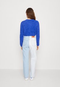 Modrý načechraný krátký svetr v kombinaci se světle modrými džínami a bílými teniskami. Svetr má texturovanou tkaninu a džínové kalhoty jsou zdobeny jemným logem.