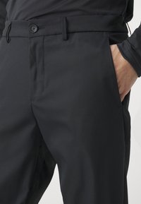 Black trousers featuring a smooth texture, tailored fit, front pockets, and a single button closure at the waist.