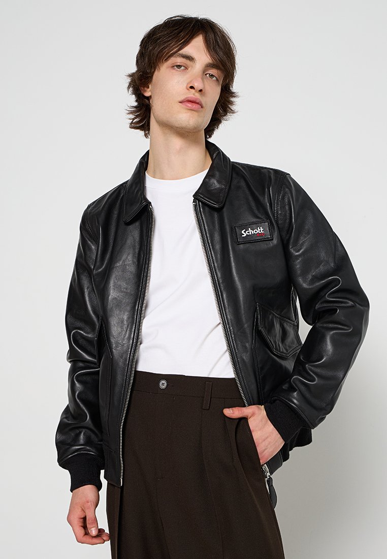 Veste bomber en cuir noir avec une fermeture éclair à l'avant, des poches latérales et un col. Dotée d'un écusson de marque rouge et blanc sur la poitrine gauche.