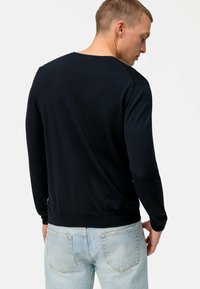 Maglione blu navy a maniche lunghe con collo a giro, polsini e orlo a coste, realizzato in tessuto morbido, mostrato dal retro con jeans in denim chiaro.