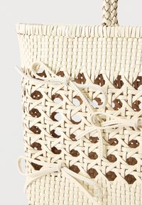 Κοντινή λήψη ενός μπεζ υφαντού καλάθι με πλεκτή λαβή και διακοσμητικά δερμάτινα φιόγκους στο πλεκτό σχέδιο.