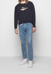 Marineblå sweatshirts med en fiskbrodering, kombinerat med ljusblå raka jeans och vita sneakers, med en klassisk rundhalsdesign.