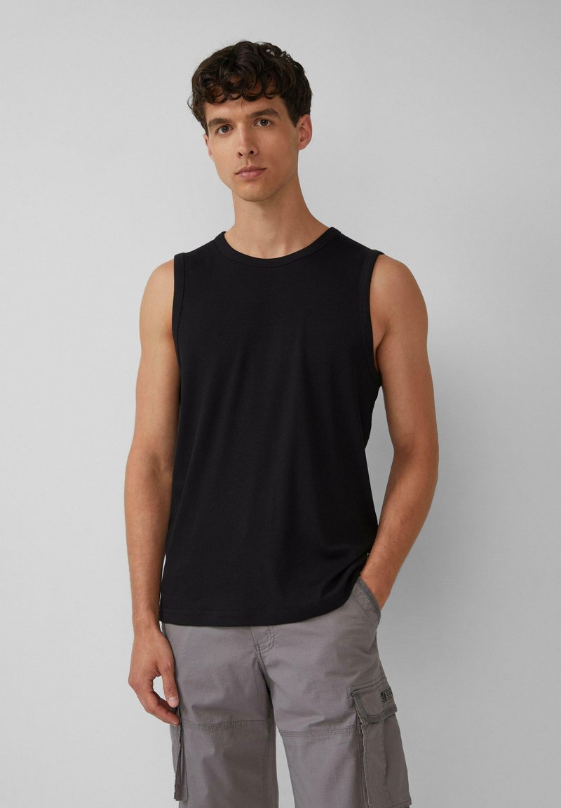 Schwarzes ärmelloses Tanktop aus glattem Stoff, mit einem runden Ausschnitt und einer figurbetonten Silhouette. Kombiniert mit grauen Cargo-Shorts.