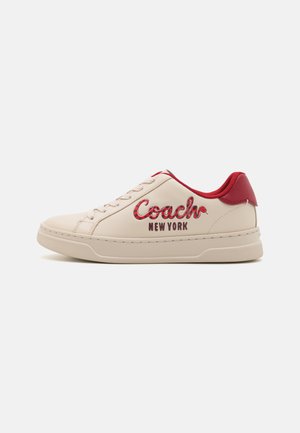 Beige leren sneaker met rode hiel en accenten. Voorzien van vetersluiting en het "Coach New York" logo in rode en zwarte letters. Getextureerde zool.