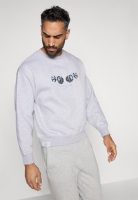 Sweatshirt cinza claro com decote redondo, punhos e barra canelados, apresentando uma estampa gráfica colorida na parte da frente. Textura suave.