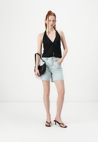 Top negro tipo halter con escote en V, shorts de mezclilla clara, bolso negro de hombro y sandalias negras de tiras. Telas suaves, estilo casual.