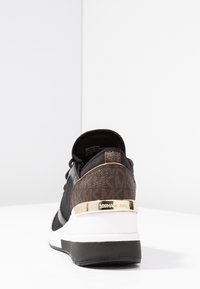 Chaussure de sport noire avec des accents marron texturés, une quincaillerie dorée et une semelle intermédiaire blanche. Dotée de lacets et d'un col rembourré.