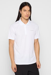 Polo blanco hecho de tejido suave, con un cuello clásico, tapeta de tres botones y un sutil logo en el lado izquierdo del pecho.