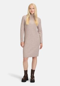 Abito a collo alto in maglia beige chiaro, con texture a coste e silhouette aderente, abbinato a stivaletti alla caviglia in pelle scura con tacco plateau.