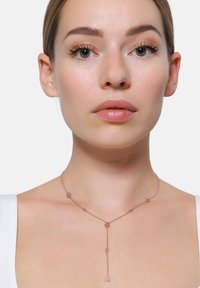 Collana in oro rosa con una delicata catena che presenta accenti ovali e a goccia, creando un effetto a strati. Superficie liscia e riflettente.