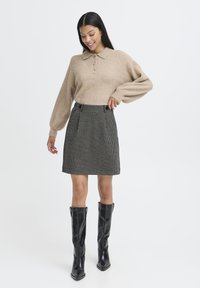 Beige striktrøje med krave og knapper, parret med en sort-hvid ternet nederdel og knæhøje sorte læderstøvler.