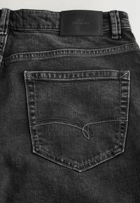 Black denim jeans with a back pocket featuring a subtle stitched design. Smooth texture with a leather brand label above the waistband.