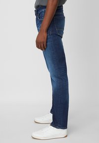 Vaqueros de mezclilla azul oscuro con un diseño de pierna recta, bolsillos laterales y costuras visibles. Llevados con zapatillas blancas.