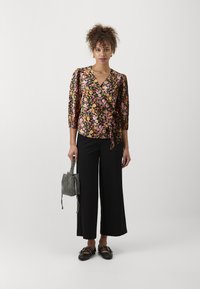 Blusa a fiori con sfondo nero, maniche 3/4 e fiocco laterale. Abbinata a pantaloni ampi neri e una borsa texture bianco e nero.