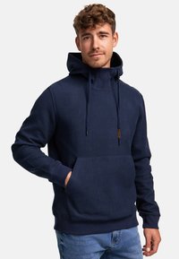 Marineblå hettegenser med teksturert mønster, stor frontlomme, lange ermer og justerbar snorhette. Laget av mykt stoff.