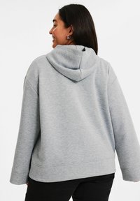 Grå huvtröja med avslappnad passform, breda ärmar och en texturerad tyg. Enkel design utan synliga logotyper eller mönster.