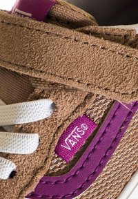 Sneaker in suede marrone con lacci bianchi, accento viola vicino al logo e corpo in tessuto texturizzato. Presenta una fascia in Velcro e dettagli cuciti.