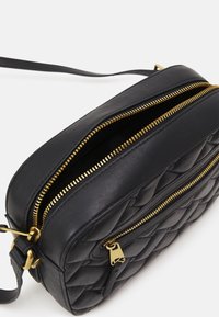 Borsa a tracolla nera in pelle con motivo trapuntato, chiusure con doppia zip dorata e tracolla regolabile. Forma rettangolare compatta.