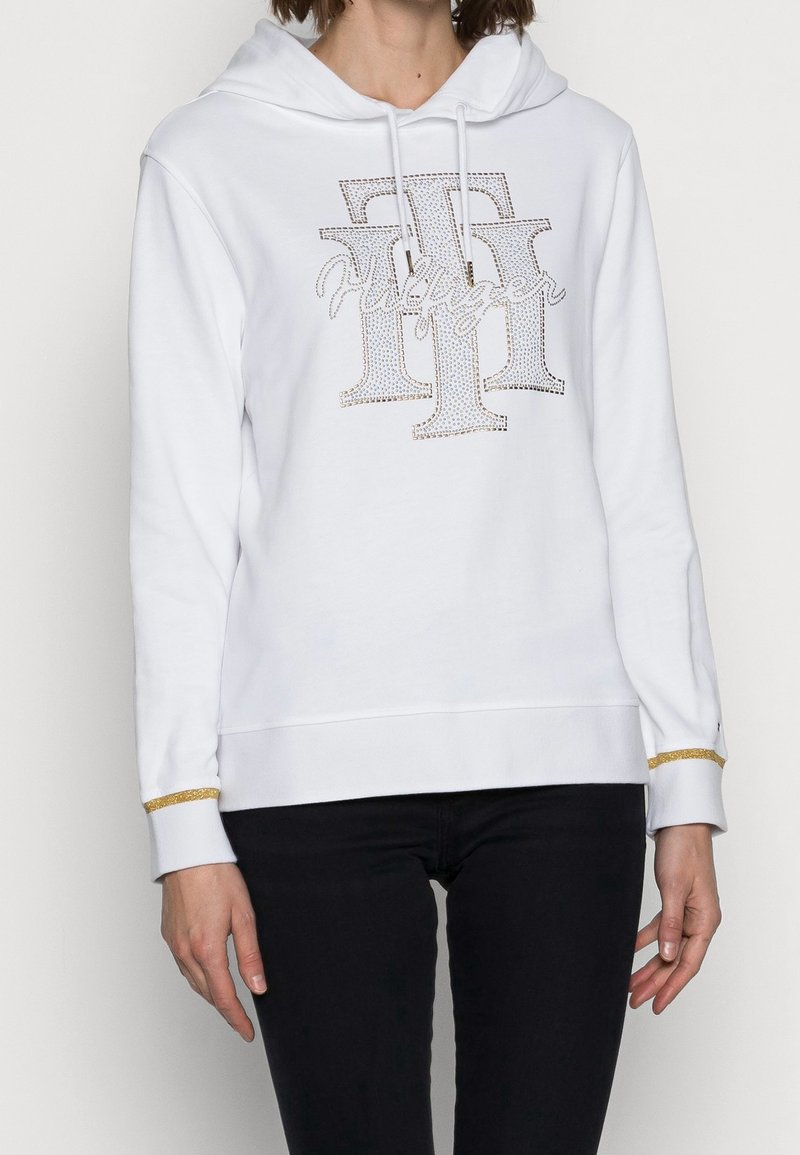 Sudadera blanca con capucha y logo de strass, con un acento dorado en los puños y un corte relajado. Tejido suave y liso, con cordones.