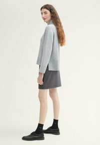 Pull en maille gris clair avec un ourlet côtelé associé à une jupe à carreaux noir et gris. Le modèle porte des chaussettes et chaussures noires.