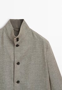 Giacca grigia chiara con texture, collo alto e cinque bottoni neri disposti lungo il davanti.