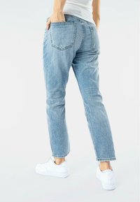 Jeans azzurri chiari a vita alta con taglio dritto, tasche posteriori visibili e dettagli leggermente scoloriti, abbinati a sneakers bianche.