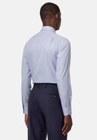 Camicia a quadri blu chiaro con maniche lunghe e colletto a punte, abbinata a pantaloni navy scuri con due tasche posteriori.